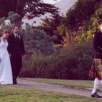 A bride, groom and bagpiper walking down a road in San Francisco